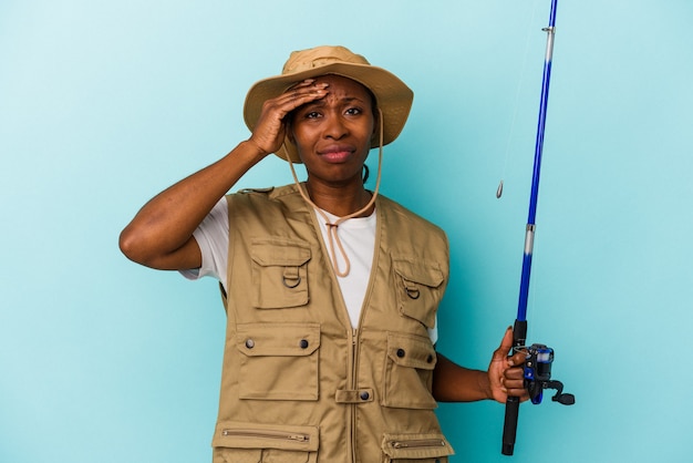 Young african american fisherwoman holding rod isolated on blue background being shocked, she has remembered important meeting.