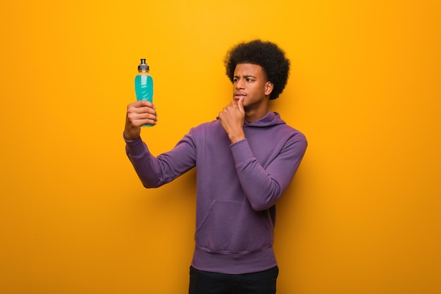 Young african american fitness man holding an energy drink doubting and confused