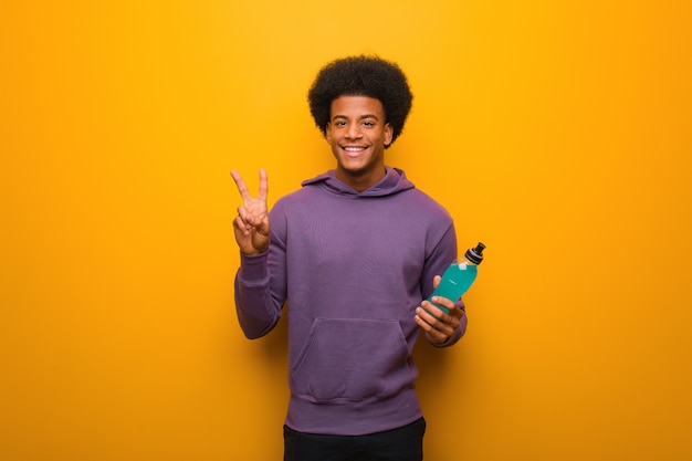 Young african american fitness man holding an energy drink fun and happy doing a gesture of victory