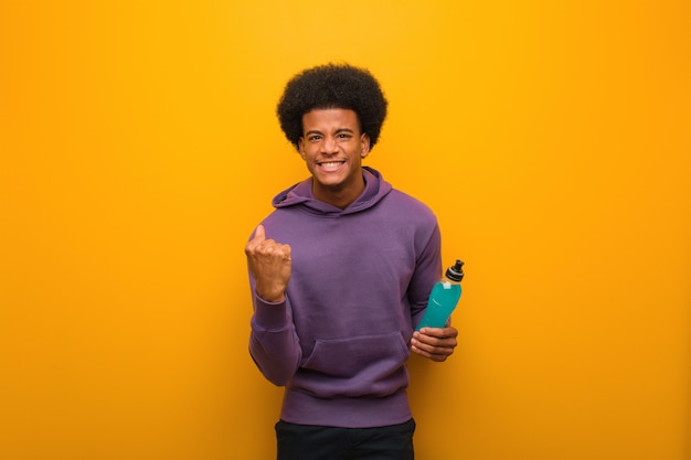 Young african american fitness man holding an energy drink surprised and shocked