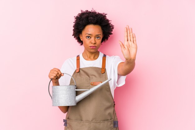 Young african american gardener woman standing with outstretched hand showing stop sign, preventing you.