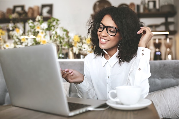 Young African American girl in glasses sitting in restaurant with laptop