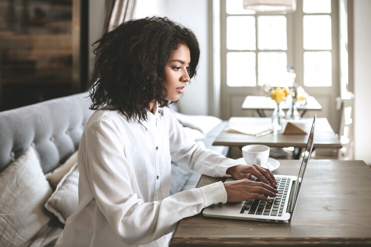 Young African American girl sitting in restaurant and typing on her laptop. Pretty girl working on computer at cafe