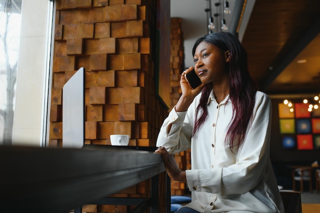 Young African American girl sitting in restaurant and typing on her laptop Pretty girl working on computer at cafe