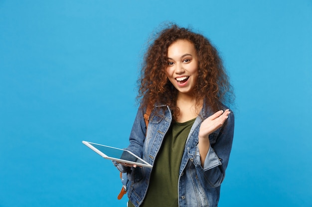 Photo young african american girl teen student in denim clothes, backpack hold pad pc isolated on blue wall wall