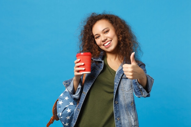 Young african american girl teen student in denim clothes, backpack hold paper cup isolated on blue wall