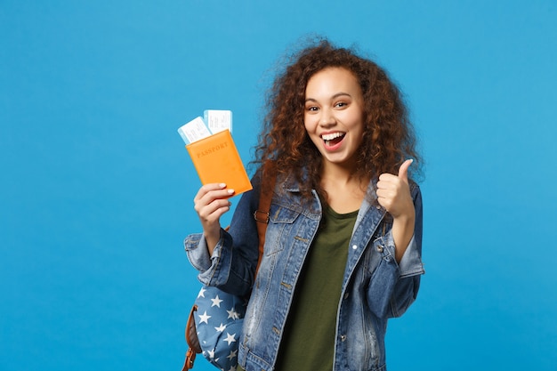 Young african american girl teen student in denim clothes, backpack hold pass isolated on blue wall