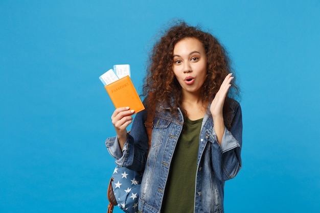 Young african american girl teen student in denim clothes, backpack hold pass isolated on blue wall