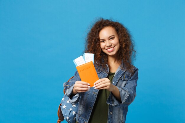 Young african american girl teen student in denim clothes, backpack hold pass isolated on blue wall