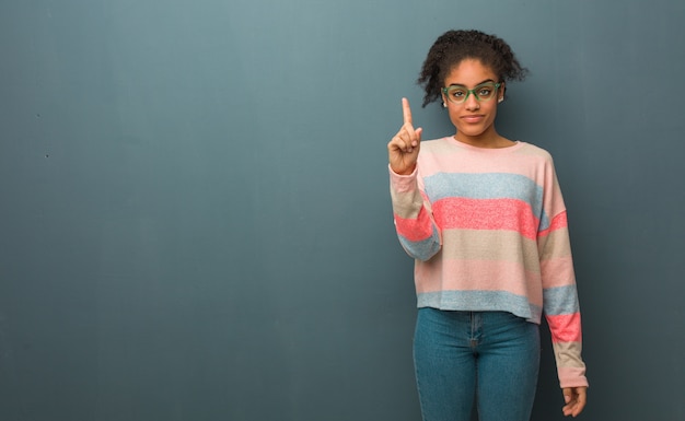 Young african american girl with blue eyes showing number one