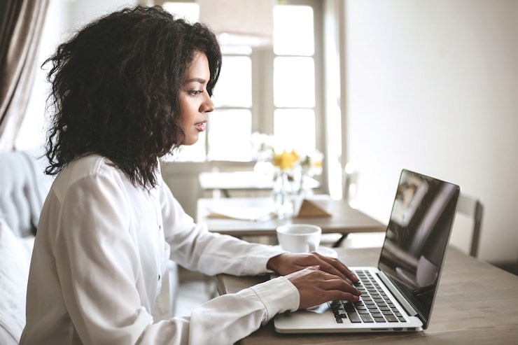 Photo young african american girl working on her laptop in restaurant.pretty lady with dark curly hair sitting at cafe with laptop