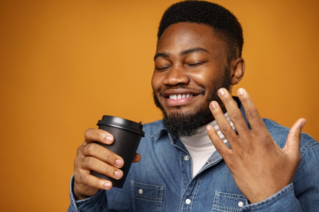 Young african american guy enjoying his takeaway cup of coffee against yellow background