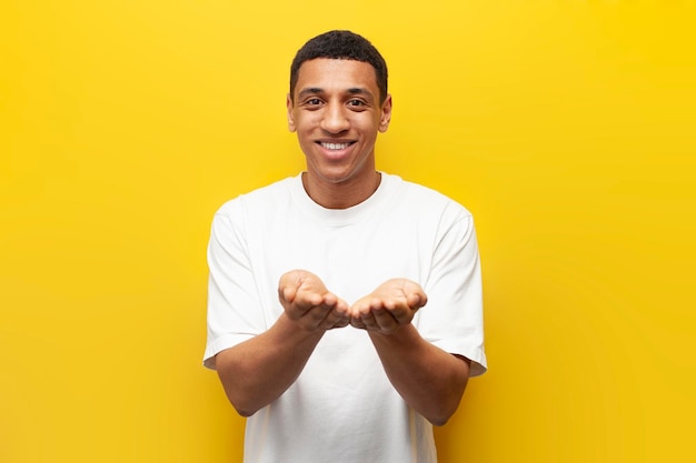 Young African American guy holds his hands in front of him on yellow background man holds nothing