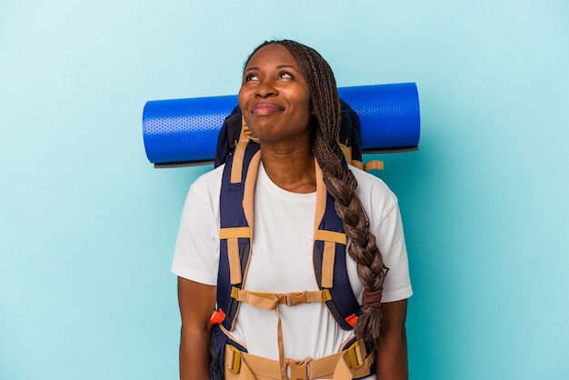 Young african american hiker woman isolated on blue background dreaming of achieving goals and purposes