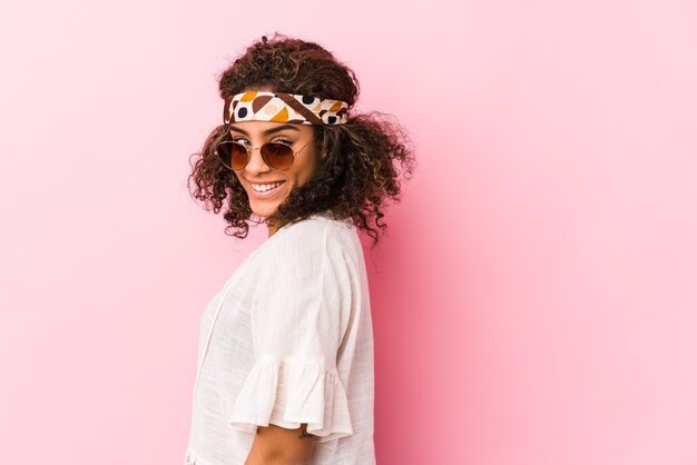 Young african american hipster woman isolated on pink background looks aside smiling, cheerful and pleasant.