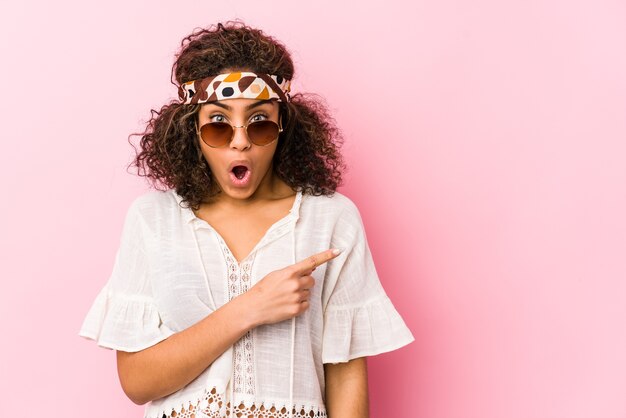 Young african american hipster woman isolated on pink wall pointing to the side