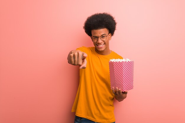 Young african american holding a popcorn bucket cheerful and smiling pointing to front