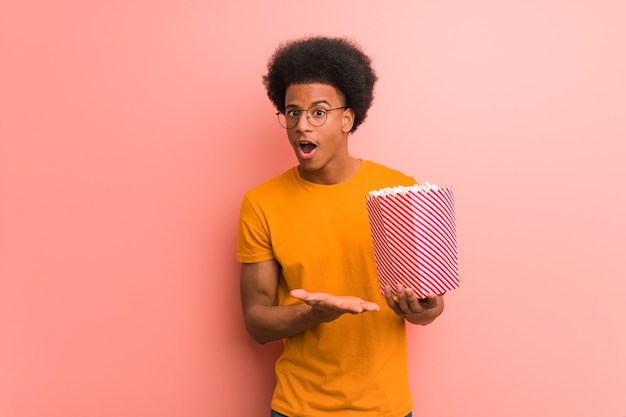 Young african american holding a popcorn bucket holding something on palm hand