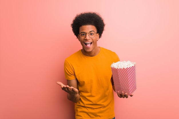 Young african american holding a popcorn bucket surprised and shocked