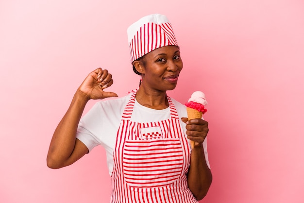 분홍색 배경에 격리된 아이스크림을 들고 있는 젊은 아프리카계 미국인 아이스크림 제조사 여성은 자부심과 자신감을 느낍니다.