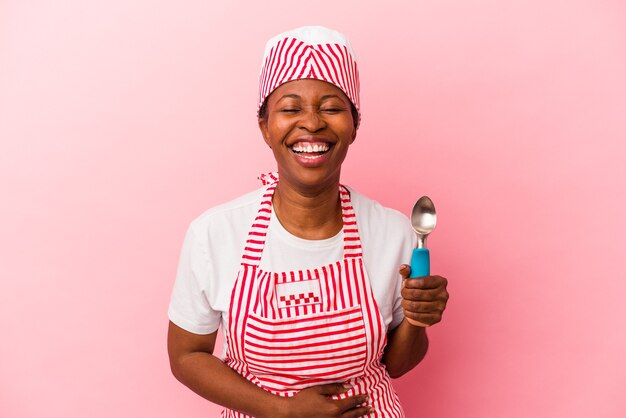 Young african american ice cream maker woman holding scoop isolated on pink background laughing and having fun.