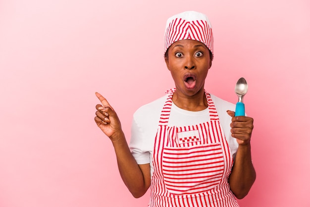 Young african american ice cream maker woman holding scoop isolated on pink background pointing to the side
