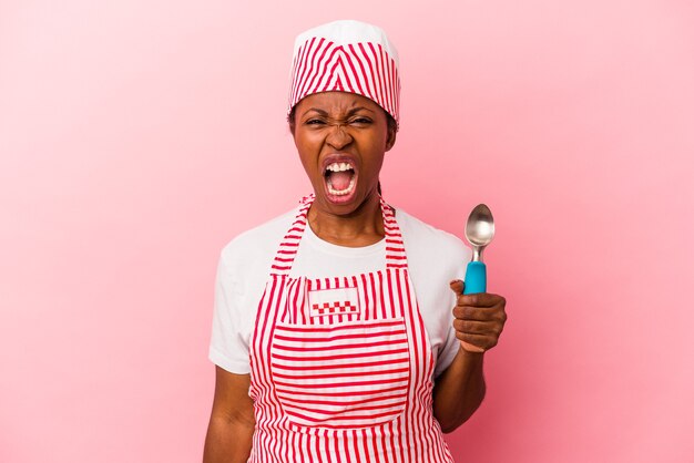 Young african american ice cream maker woman holding scoop isolated on pink background screaming very angry and aggressive.