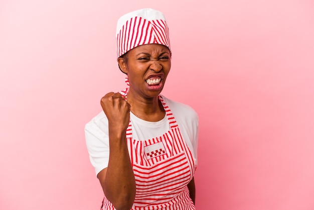 Young african american ice cream maker woman isolated on pink background showing fist to camera, aggressive facial expression.