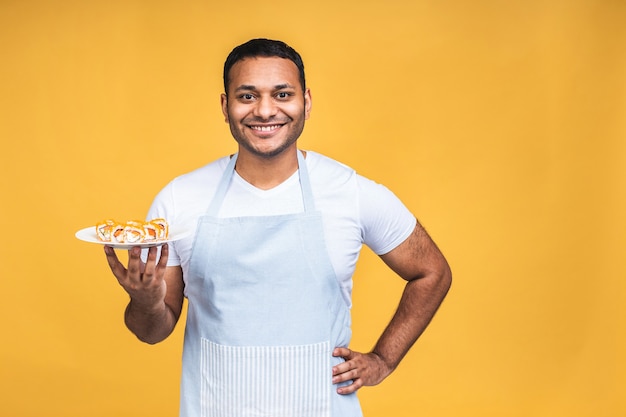 Giovane uomo nero indiano afroamericano che mangia sushi usando le bacchette sopra fondo giallo isolato. cuoco preparando il sushi.