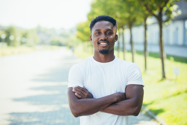 Il giovane atleta maschio afroamericano, durante una corsa mattutina, guarda la telecamera con le braccia incrociate, motivato e sorridente