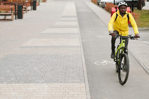 Young african american male courier with backpack riding bicycle