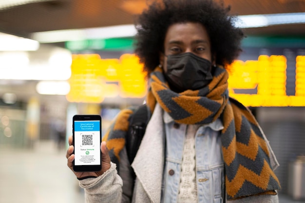 Young African American male showing his digital vaccination certificate at airport. Selective focus. Covid passport for travel.