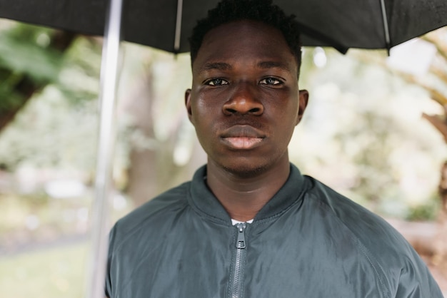 Young African American man under black umbrella in rain sad Fall or spring weather