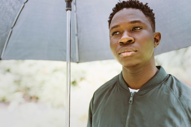 Young african american man under black umbrella in rain sad\
fall or spring weather