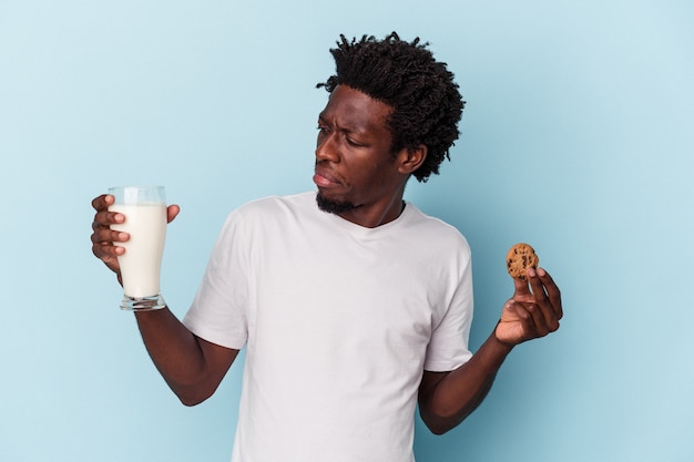 Giovane uomo afroamericano che mangia biscotti con gocce di cioccolato e beve latte su blue