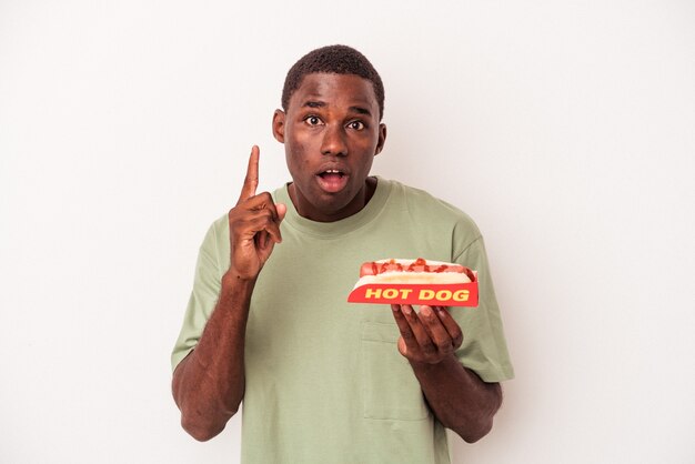 Young African American man eating a hot dog isolated on white background having an idea, inspiration concept.