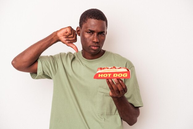 Young African American man eating a hot dog isolated on white background showing a dislike gesture, thumbs down. Disagreement concept.