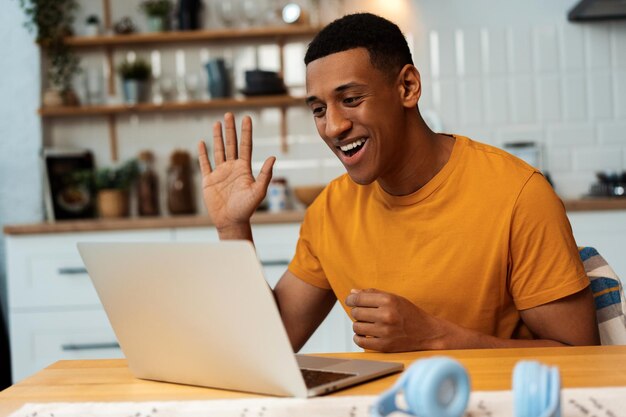 Young African American man freelancer working on computer using laptop video call waving hand