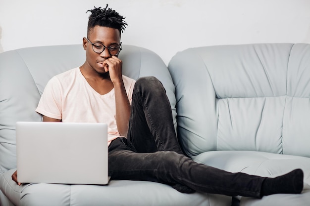 Photo young african american man in glasses sitting with laptop on sofa