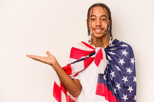 Молодой афроамериканец, держащий американский флаг на белом фоне, показывает место для копирования на ладони и держит другую руку на талии