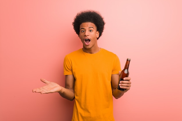 Young african american man holding a beer celebrating a victory or success