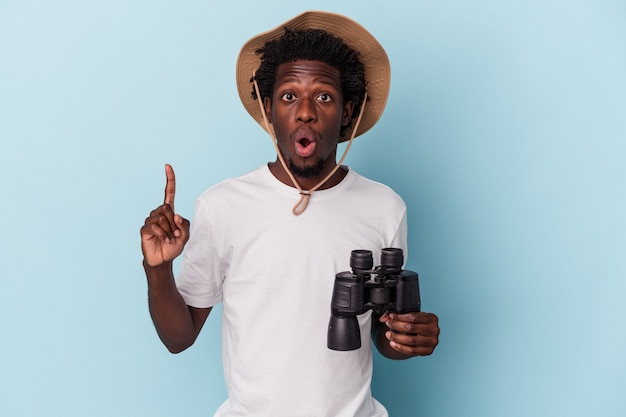 Young african american man holding binoculars isolated on blue background having some great idea, concept of creativity.