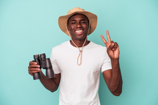 Young African American man holding binoculars isolated on blue background showing number two with fingers