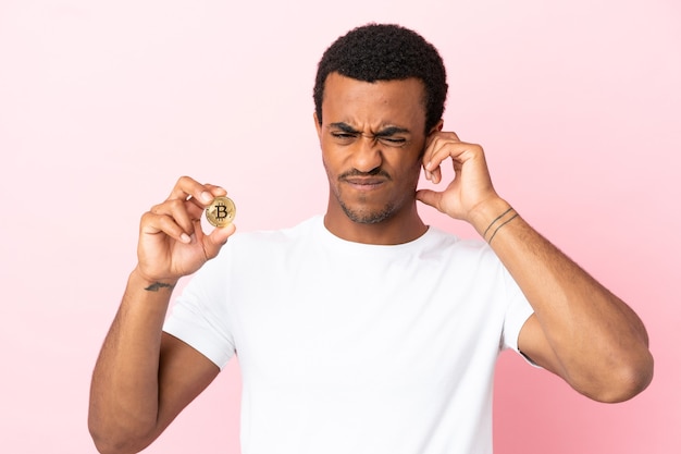 Young African American man holding a Bitcoin over isolated pink background frustrated and covering ears