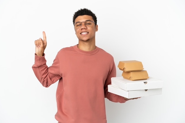 Young African American man holding a burger and pizzas isolated on white background showing and lifting a finger in sign of the best