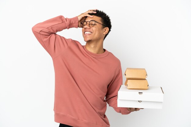 Young African American man holding a burger and pizzas isolated on white background smiling a lot