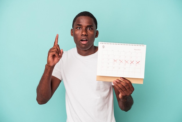 Young African American man holding a calendar isolated on blue background having an idea, inspiration concept.