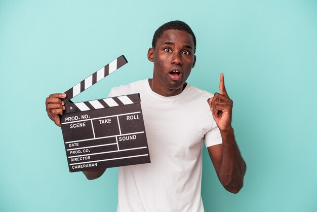 Young African American man holding clapperboard isolated on blue background having an idea, inspiration concept.