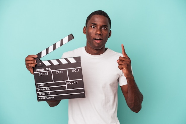 Young African American man holding clapperboard isolated on blue background having some great idea, concept of creativity.