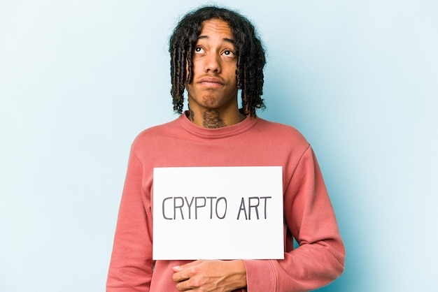 Young African american man holding crypto art placard isolated on blue background dreaming of achieving goals and purposes